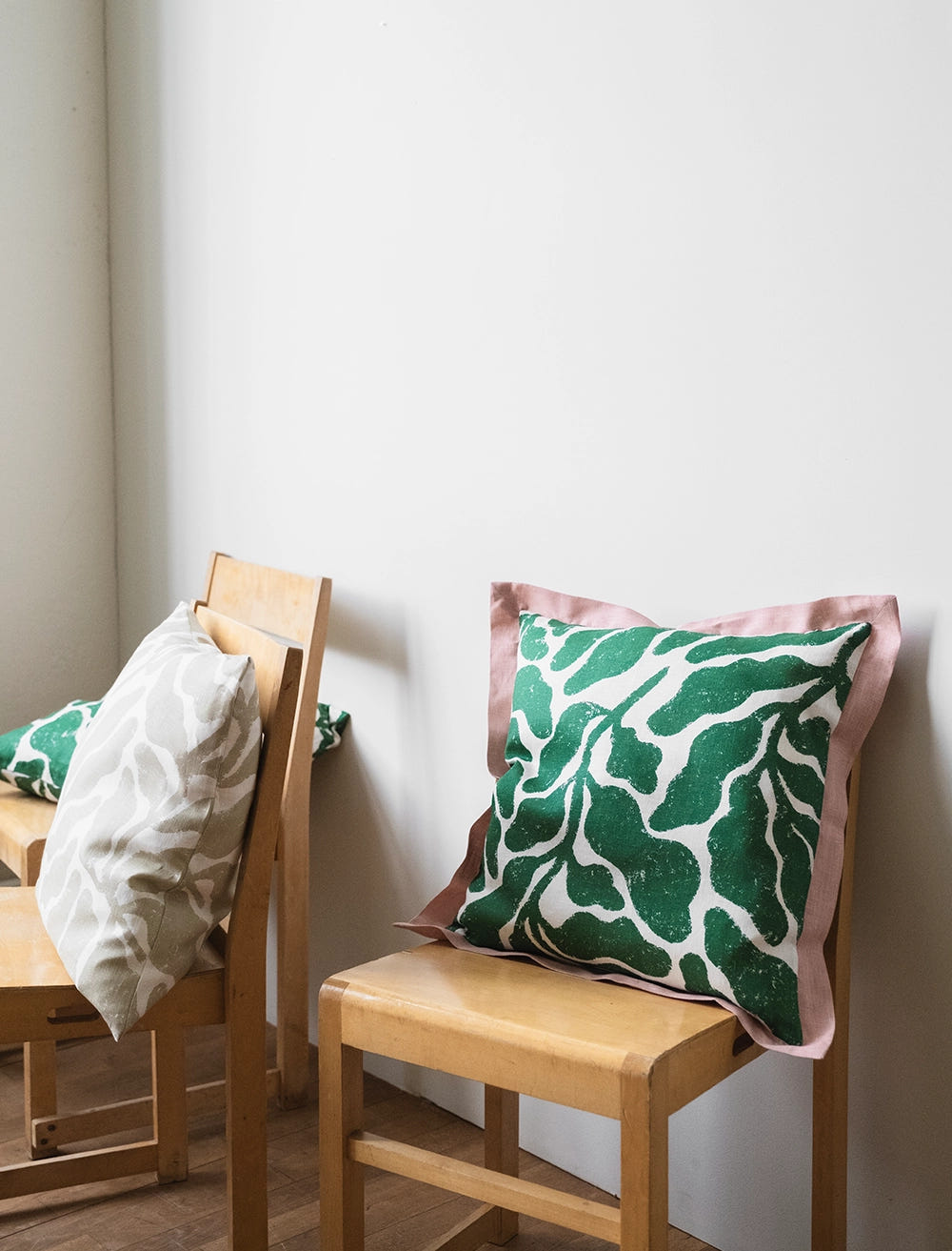 Kuddfodral med stort grönt bladmönster och en rosa volang runt omkring stående på en stol