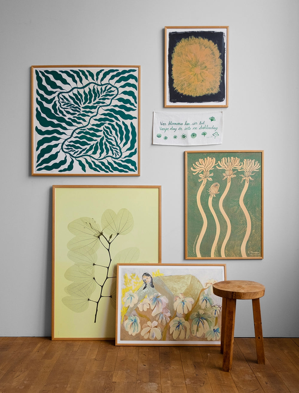 En tavelvägg med posters i grönt och gult. Framför står en trefotad träpall.