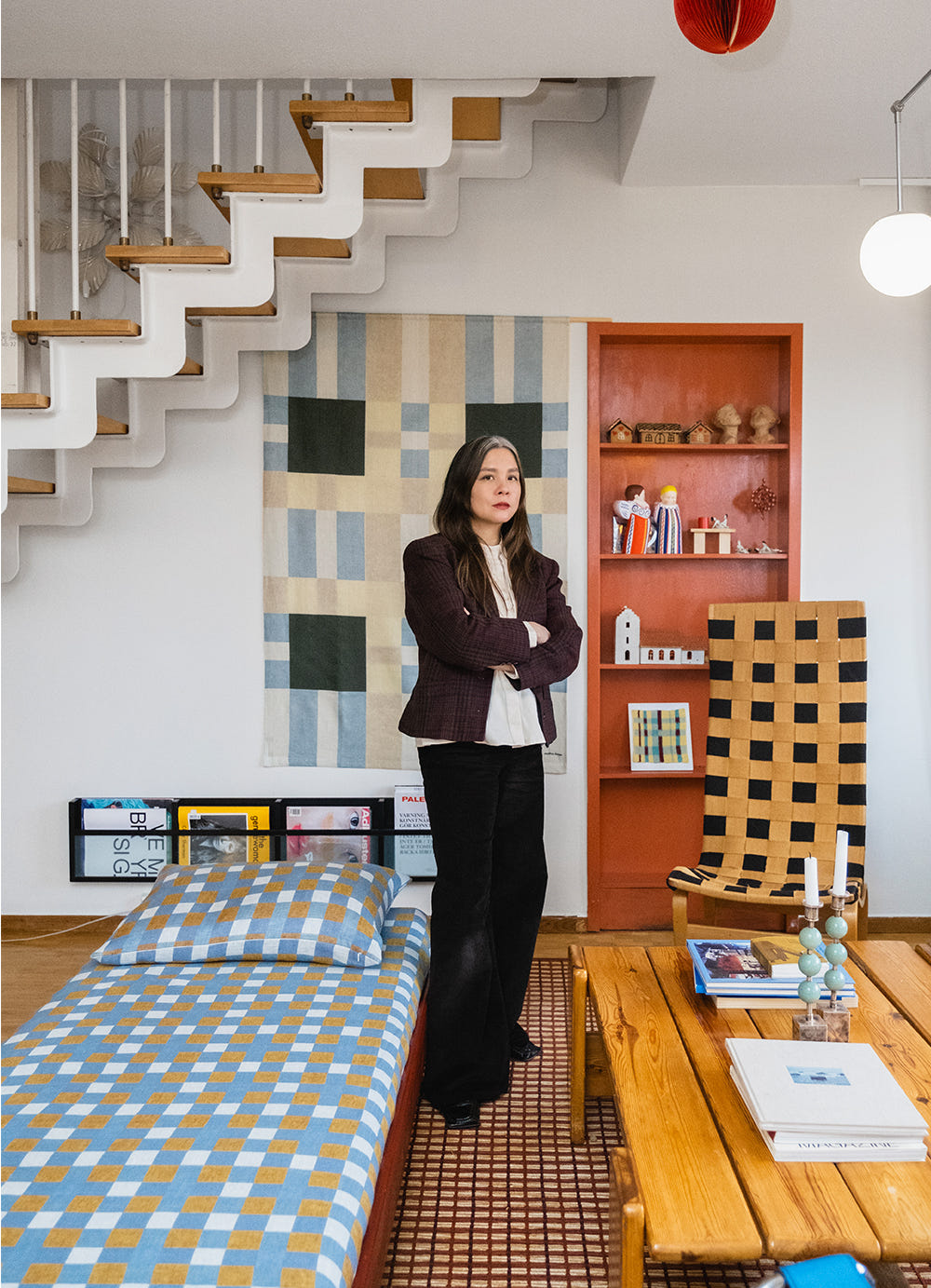 Konstnären står i ett rum framför en väggbonad med stort grafiskt rutmönster i blått, gult och mörkgrönt.